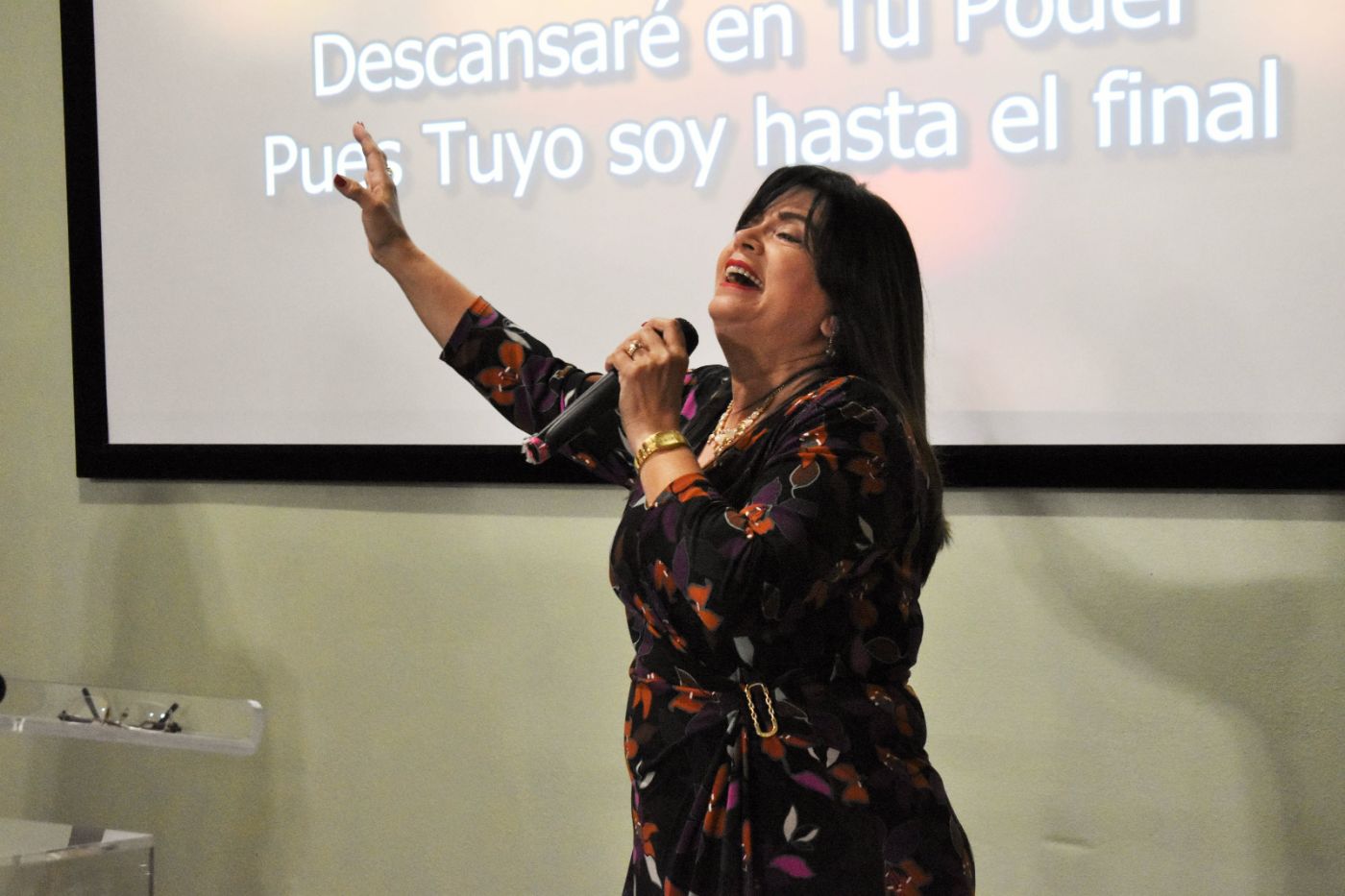 Woman speaking at podium with microphone in front of projected Spanish text on screen