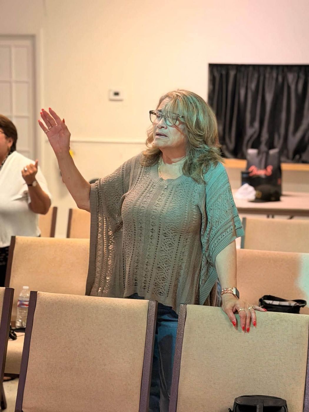 Woman with glasses speaking with raised hand in conference room with beige chairs