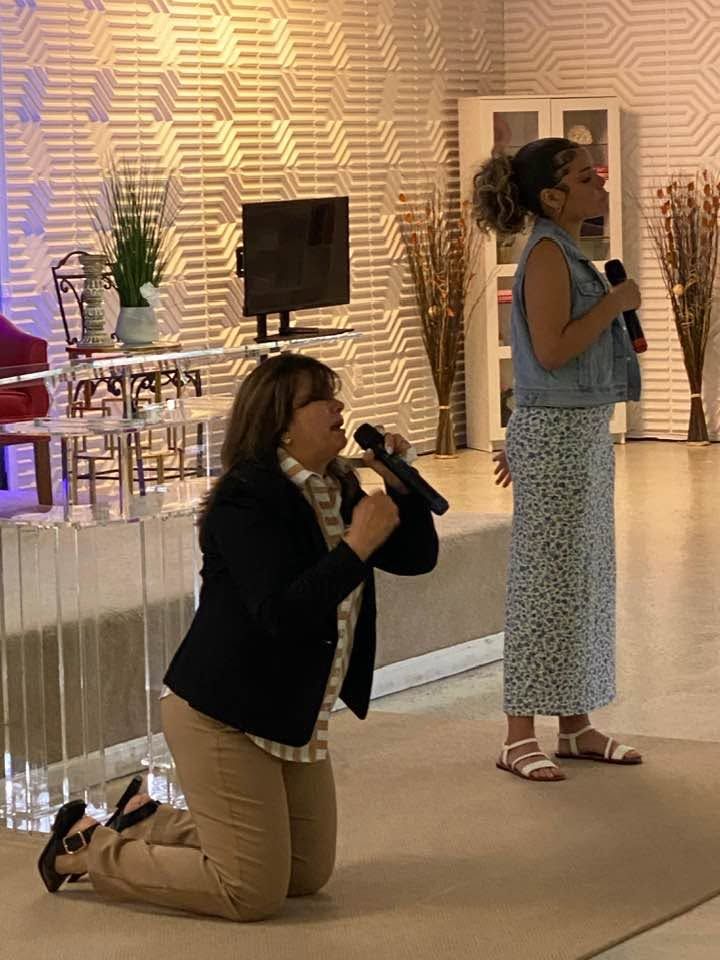 Woman kneeling with microphone speaking to standing woman in modern office interior with textured wall