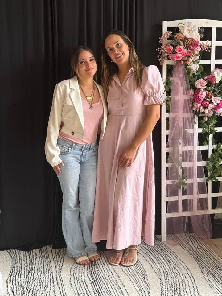 Two women posing together in front of a floral archway with pink and white flowers
