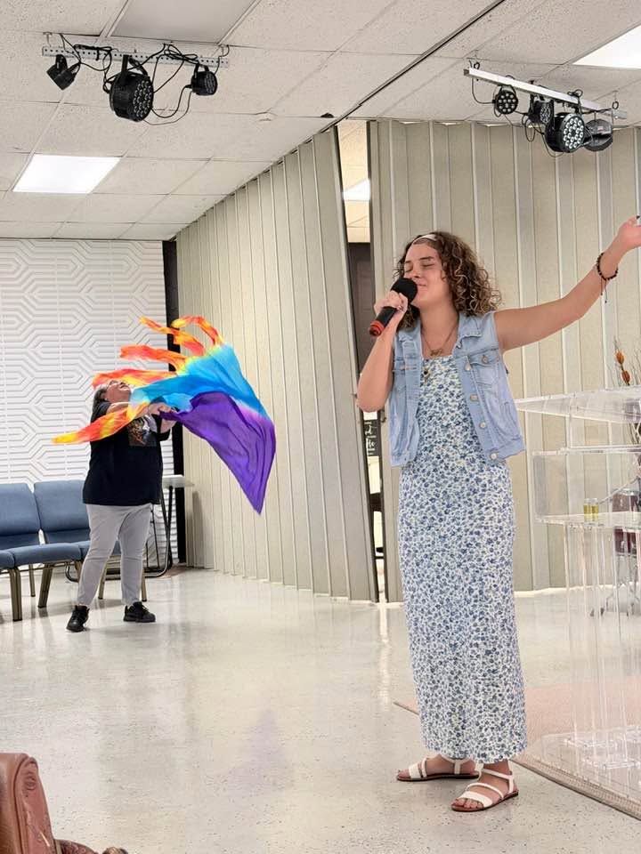 Woman speaking into microphone at indoor event with colorful rainbow flag prop